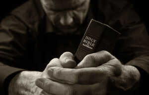 A Man praying holding a Holy Bible.